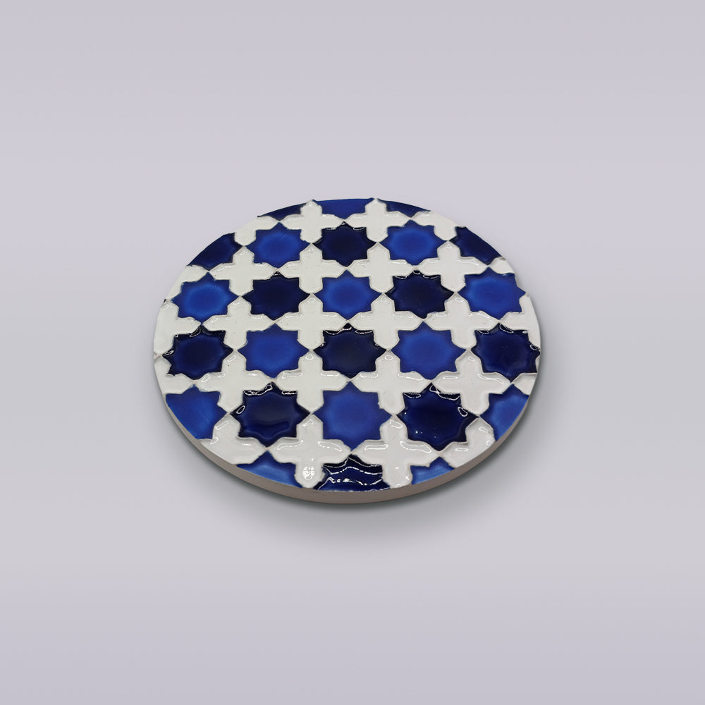 The Heritage Blue Star Mosaic Coaster by Miradouro Ceramics is a round ceramic piece featuring interlocking blue and white star motifs on a light background, inspired by hand-painted azulejo mosaic decor.