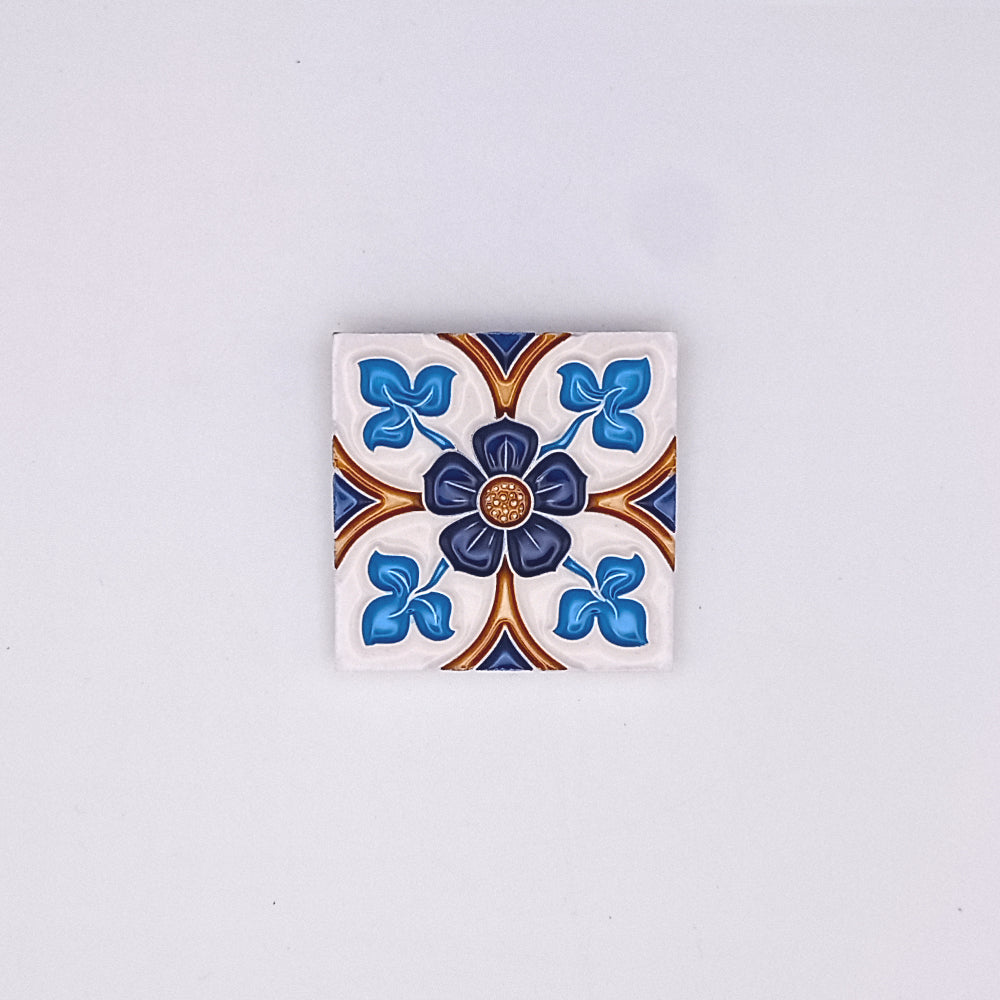 A decorative Tejo Shop Portuguese art tile featuring a symmetrical floral design in blue, white, and brown, centered with a small golden embellishment, against a plain light gray background.