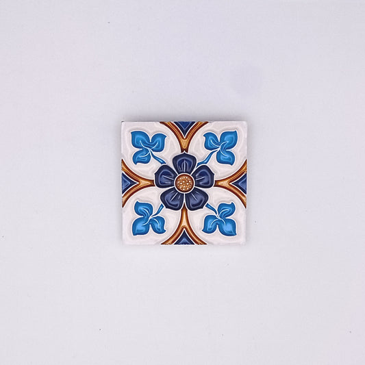 A decorative Tejo Shop Portuguese art tile featuring a symmetrical floral design in blue, white, and brown, centered with a small golden embellishment, against a plain light gray background.