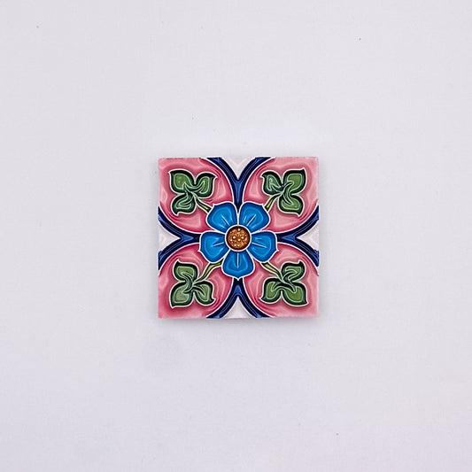 Decorative Spanish Tiles from Tejo Shop featuring a colorful floral design with blue, pink, and green petals, centered around a small orange dot, against a grey background, adding an artistic flair.