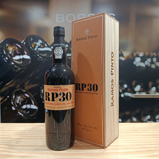 A bottle of Ramos Pinto 30 Year Old Tawny Porto stands beside its matching wooden box, both marked "RP30," while blurred Douro wine bottles complete the refined display in the background.