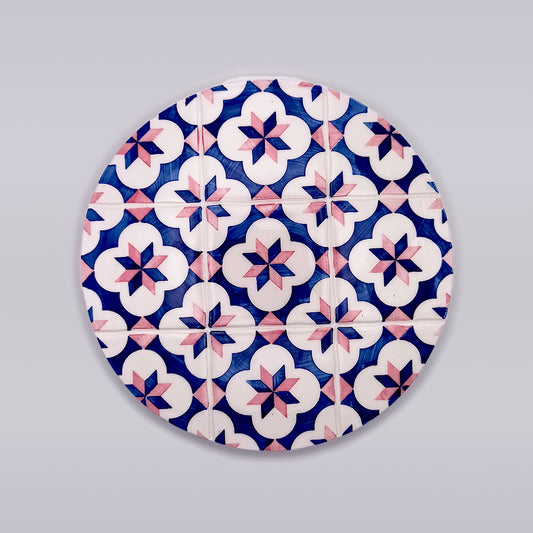 A round **Alfama Ceramic Tile Trivet** by **Tejo Shop**, showcasing a geometric pattern of blue, white, and pink star-shaped and flower-like designs, reminiscent of Algarve decor tiles. The background is a solid light grey.