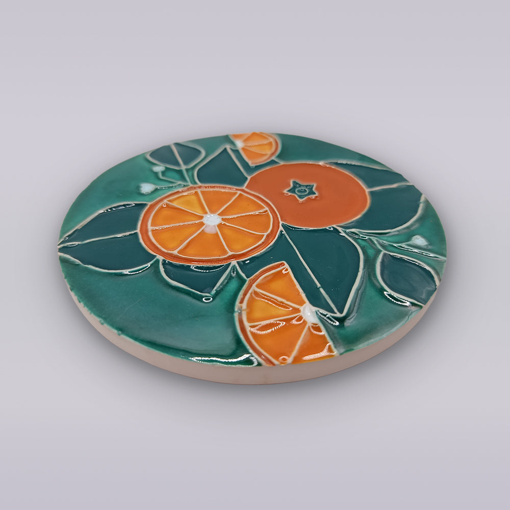 The Algarve Citrus Grove Ceramic Coaster by Miradouro Ceramics features a round Portuguese design with stylized orange slices and teal leaves—perfect for brightening your citrus-themed decor.