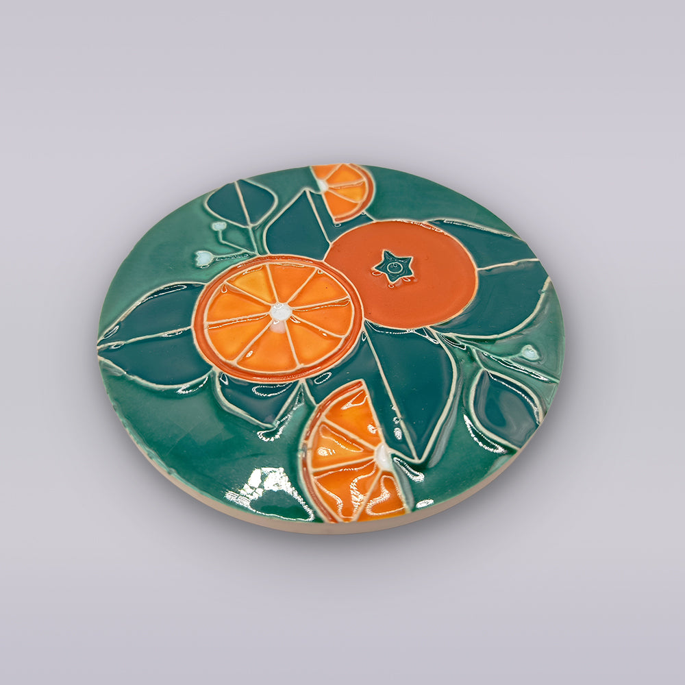 The Algarve Citrus Grove Ceramic Coaster by Miradouro Ceramics features glossy Portuguese ceramic with orange citrus slices and green leaves on a teal background—ideal for adding citrus grove style to your decor.