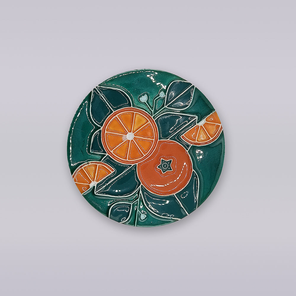 The Algarve Citrus Grove Ceramic Coaster by Miradouro Ceramics features hand-painted orange slices and green leaves on a dark green background—an ideal accent for citrus grove decor.