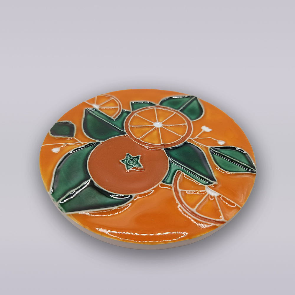 The Algarve Orange Blossom Ceramic Coaster by Miradouro Ceramics showcases a glossy, raised design of an orange fruit with green leaves and slices on an orange background.