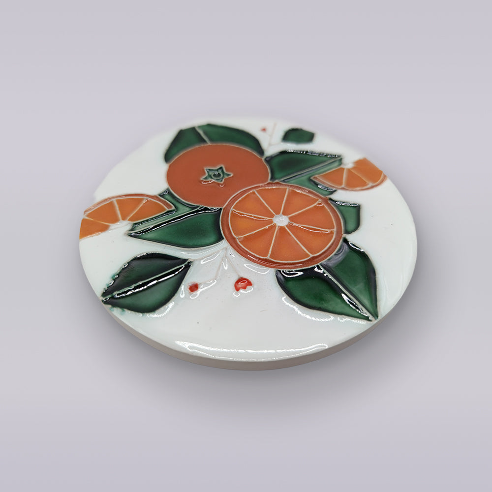 The Algarve Orange Harvest Ceramic Coaster by Miradouro Ceramics features an embossed design of oranges, slices, and green leaves on a crisp white background.