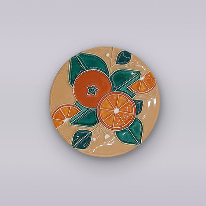 The Algarve Sandstone Orange Ceramic Coaster by Miradouro Ceramics features an orange and green geometric design of whole and sliced oranges with leaves on beige, echoing the style of a handmade Portuguese artisan piece.