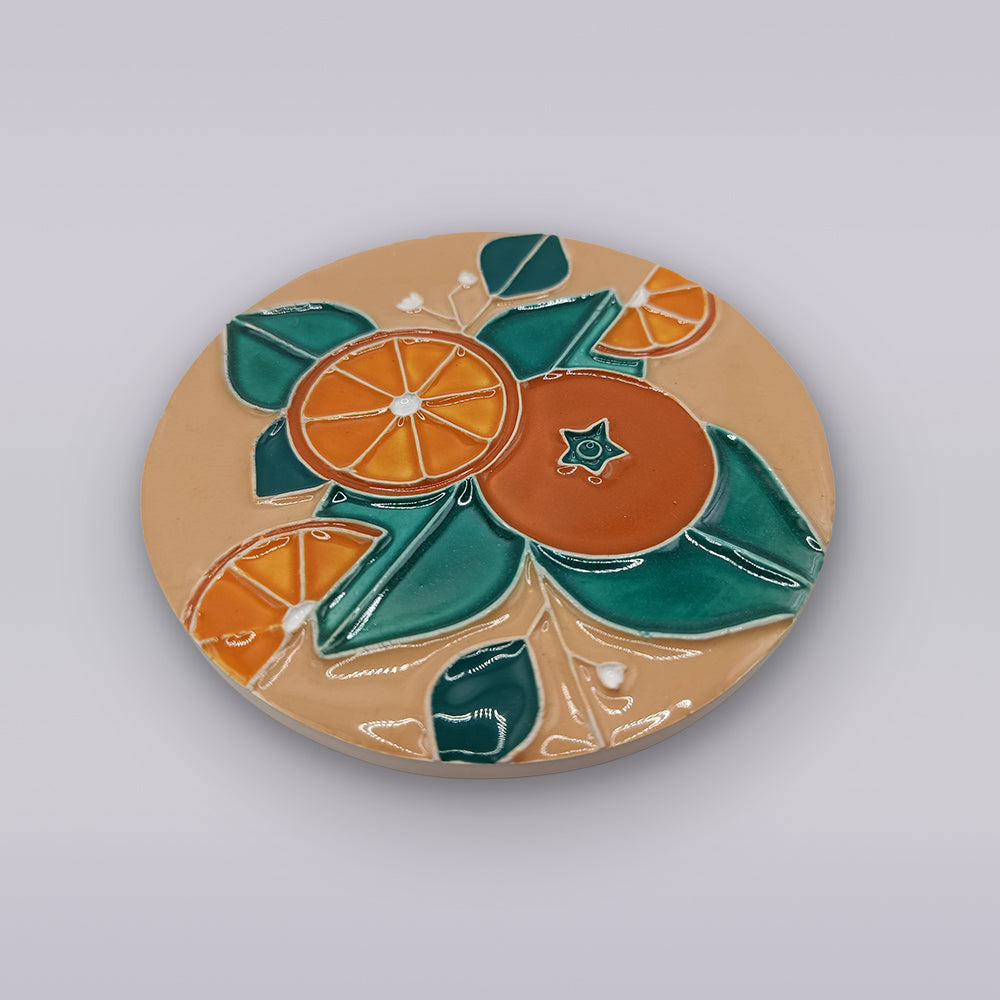 The Miradouro Ceramics Algarve Sandstone Orange Ceramic Coaster features raised oranges, orange slices, and green leaves on a beige background.