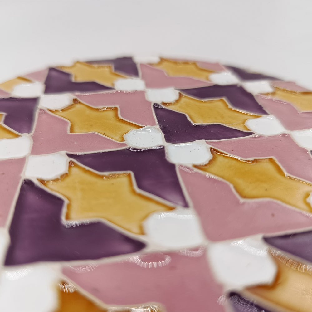 A close-up of Azulejo Pop by Miradouro Ceramics shows a glossy, colorful tile with repeating geometric star shapes in yellow, purple, pink, and white, echoing the style of Portuguese ceramics and the look of a handmade ceramic coaster.