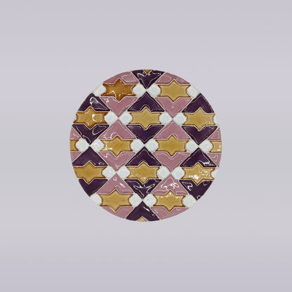 The Azulejo Pop by Miradouro Ceramics is a round handmade ceramic tile coaster featuring a geometric pattern of interlocking diamonds and star shapes in purple, gold, pink, and white, inspired by Portuguese ceramics on a light gray background.