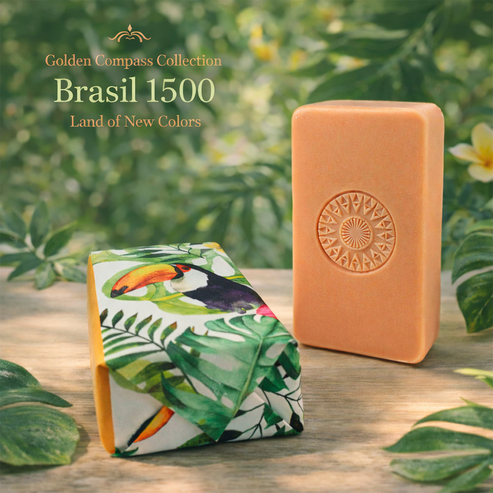 Two orange soaps are pictured: one upright with a circular embossed design, the other wrapped in paper featuring a toucan and tropical leaves. Text: "100ml Brasil 1500 – Land of New Colors.