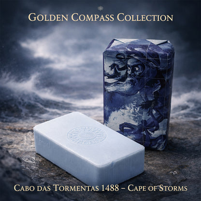 Two rectangular soaps rest on stone: one, wrapped in art of a bearded sailor and stormy sea; the other, unwrapped, pale blue, stamped with a compass. Scented marine accord & sandalwood. 100ml Cabo das Tormentas 1488 – Cape of Storms.