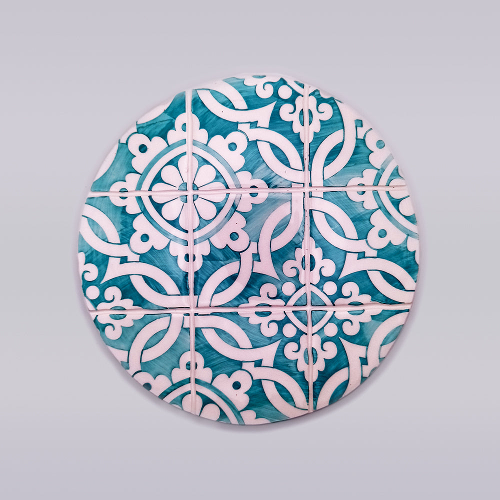 A circular arrangement of blue and white decorative tiles featuring intricate patterns of interwoven, stylized floral and geometric designs. This hand-painted **Carcavelos Ceramic Table Trivet** from **Tejo Shop** forms a symmetrical motif across the entire circle, creating a visually appealing and harmonious artisanal kitchen accessory.