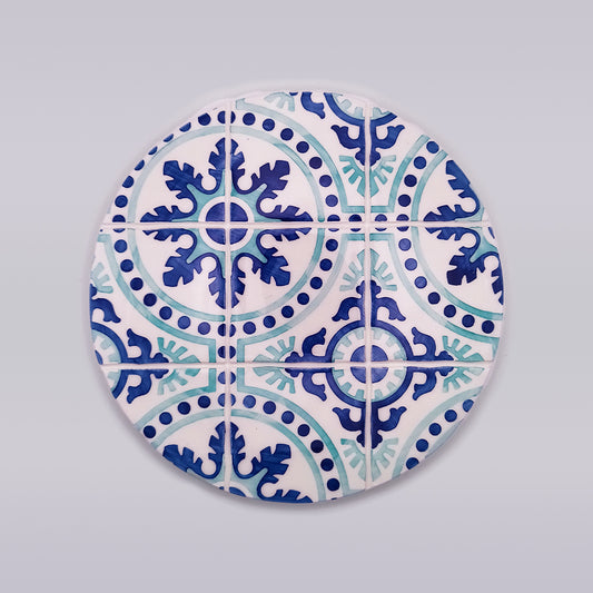 A circular mosaic tile design featuring intricate blue and teal patterns. The design includes symmetrical floral and geometric shapes, with a central star-like motif surrounded by leafy elements, bordered by dots and curved lines. This Chaves Ceramic Tile Trivet from Tejo Shop offers both artistic beauty and heat protection for your kitchen.