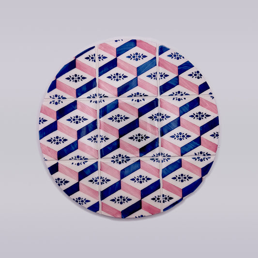A circular ceramic plate featuring a geometric pattern. The design includes blue and pink hexagons interlocking with each other, and small floral motifs inside some of the hexagons, creating a visually intricate and colorful effect against a white background, perfect as an Evora Ceramic Trivets for Hot Dishes by Tejo Shop.