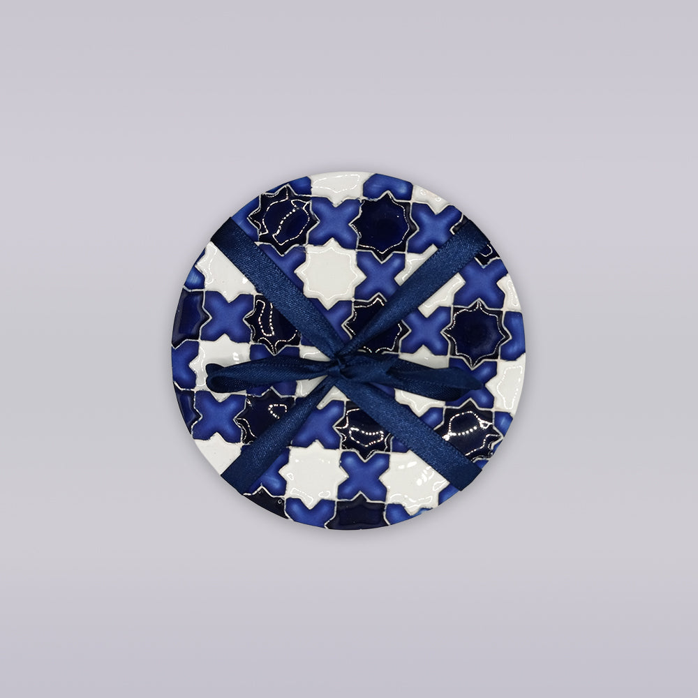 The Évora Star Azulejo Coaster by Miradouro Ceramics features a blue and white geometric design, tied with a dark blue ribbon, set on a light gray background—perfect as handmade home décor.