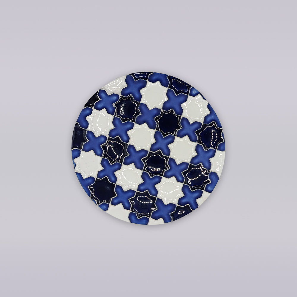 The Évora Star Azulejo Coaster by Miradouro Ceramics is a round ceramic piece featuring interlocking navy, white, and light blue star and cross patterns with gold outlines—ideal as handmade home decor.