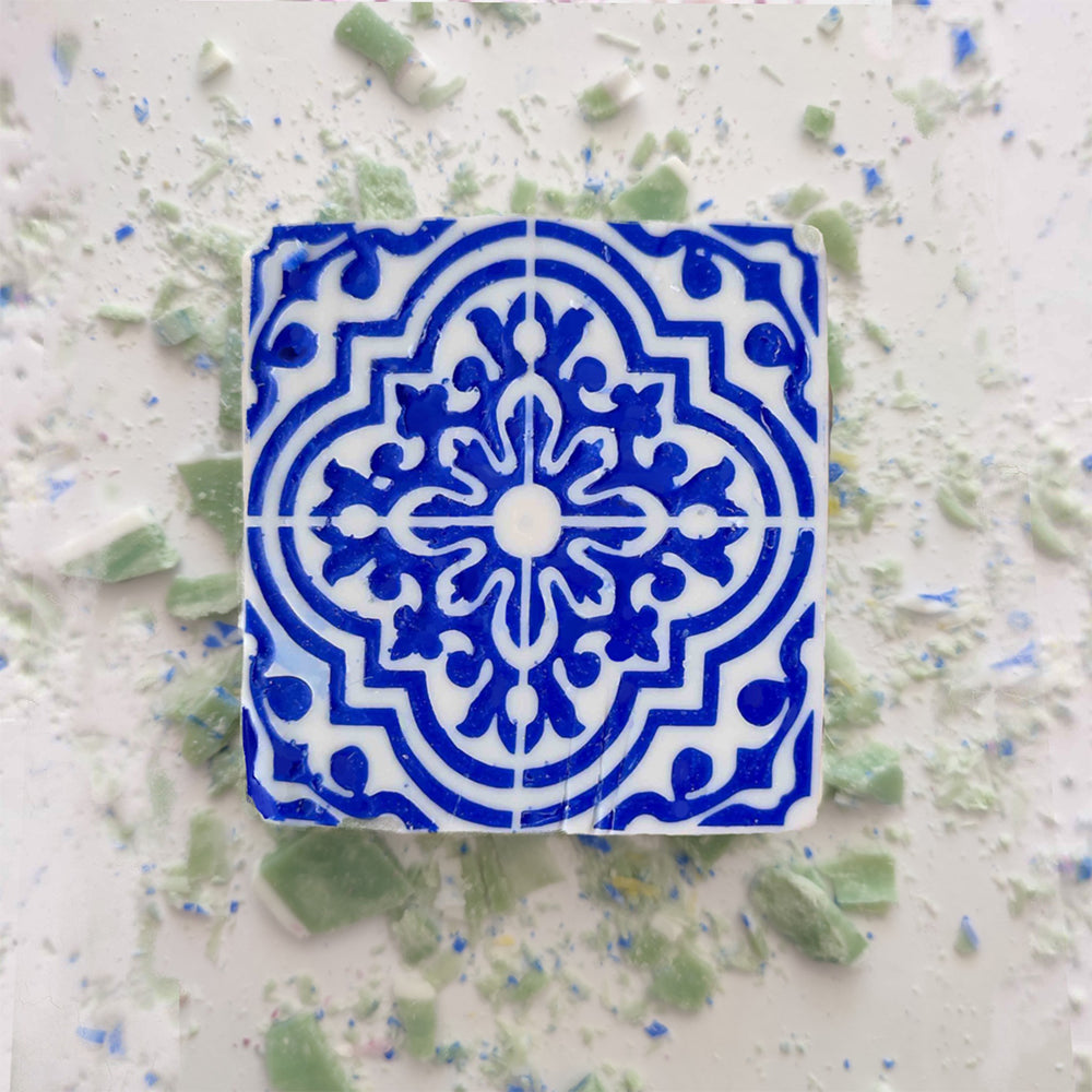 A Lisbão Mosaico Azul Green Tea Soap, featuring a blue and white geometric ceramic tile design, sits among green and blue tile shards and handcrafted soap powder.