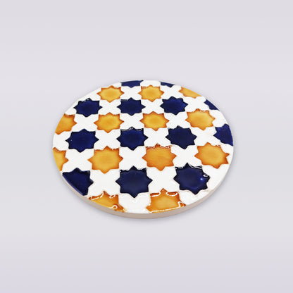 The Heritage Star Mosaic Coaster by Miradouro Ceramics is a round Portuguese ceramic coaster featuring Mudéjar star patterns with navy blue, yellow-orange, and white crosses on a white background.
