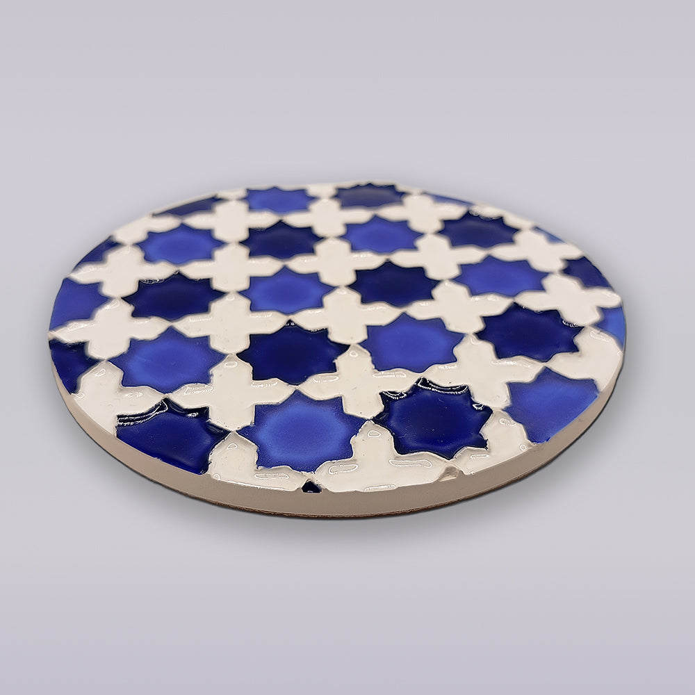 The Heritage Blue Star Mosaic Coaster by Miradouro Ceramics is a round Portuguese ceramic featuring interlocking blue and white geometric patterns, inspired by traditional azulejo mosaics on a light gray background.