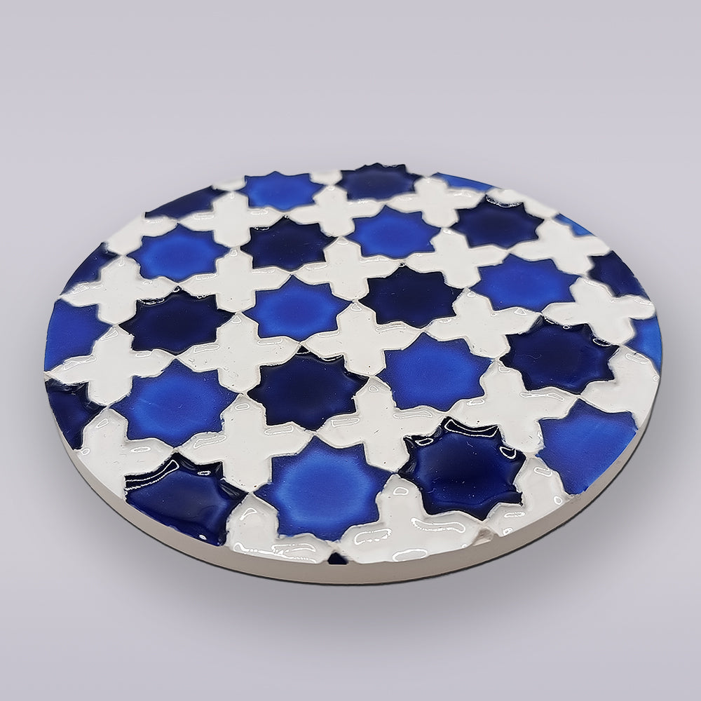 The Heritage Blue Star Mosaic Coaster by Miradouro Ceramics is a round Portuguese ceramic coaster with interlocking blue and white stars in an azulejo-inspired geometric pattern, featuring glossy raised surfaces on a light grey background.