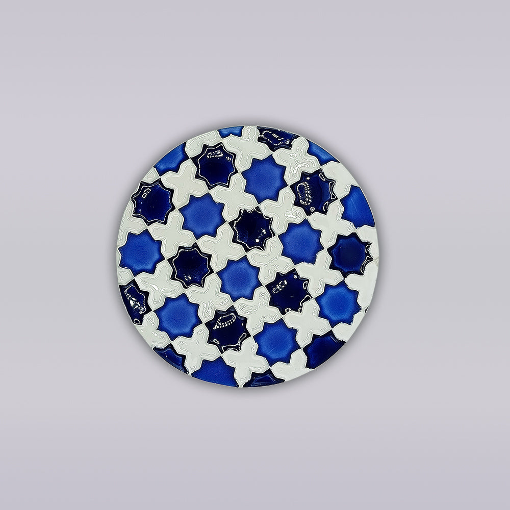 The Heritage Blue Star Mosaic Coaster by Miradouro Ceramics features a symmetrical, azulejo-inspired pattern of interlocking blue and white shapes on a round form, set against a plain light gray background.