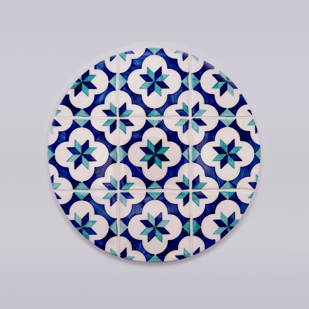 A Tejo Shop hand-crafted Lisbon Ceramic Trivet for Hot Pods with a geometric pattern featuring white, blue, and teal star shapes within blue and white flower-like designs, set against a light gray background. Perfect as kitchen decor, the symmetrical pattern gives it a vibrant and intricate appearance.