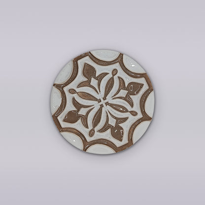 The Lusitana TerraFleur by Miradouro Ceramics is a round ceramic tile featuring intricate brown and white floral and geometric patterns on light gray, inspired by Portuguese handcrafted decorative tile traditions.