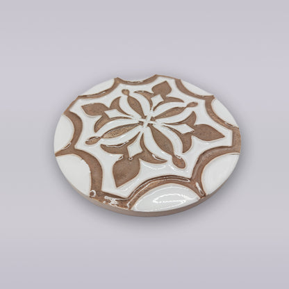 The Lusitana TerraFleur by Miradouro Ceramics is a round ceramic coaster with a raised floral and geometric motif in white and light brown on a light gray background, inspired by Portuguese handcrafted tile designs.