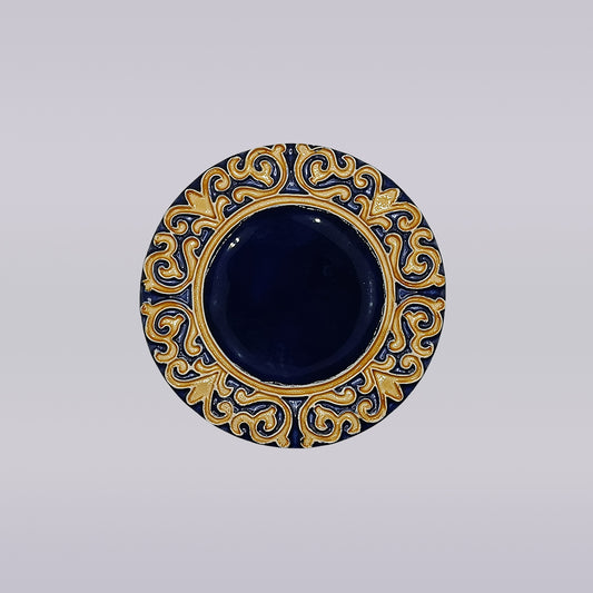 The Manuel I Royal Crest Ceramic Coaster by Miradouro Ceramics features a round shape with a deep blue center and an ornate gold and blue border inspired by Manueline art, set on a light neutral background.