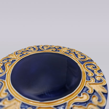 The Manuel I Royal Crest Ceramic Coaster by Miradouro Ceramics features a deep blue center and intricate gold and blue rim, inspired by Manueline art, displayed against a light gray background.