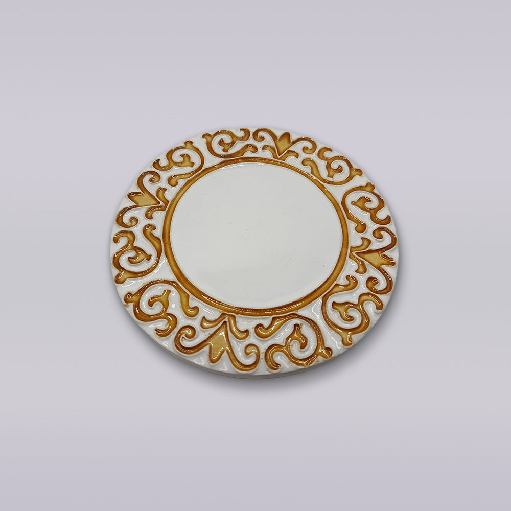 The Miradouro Ceramics Manueline Golden Crest Ceramic Coaster features an ornate gold pattern inspired by Portuguese decor on a round white surface, displayed against a simple light background.