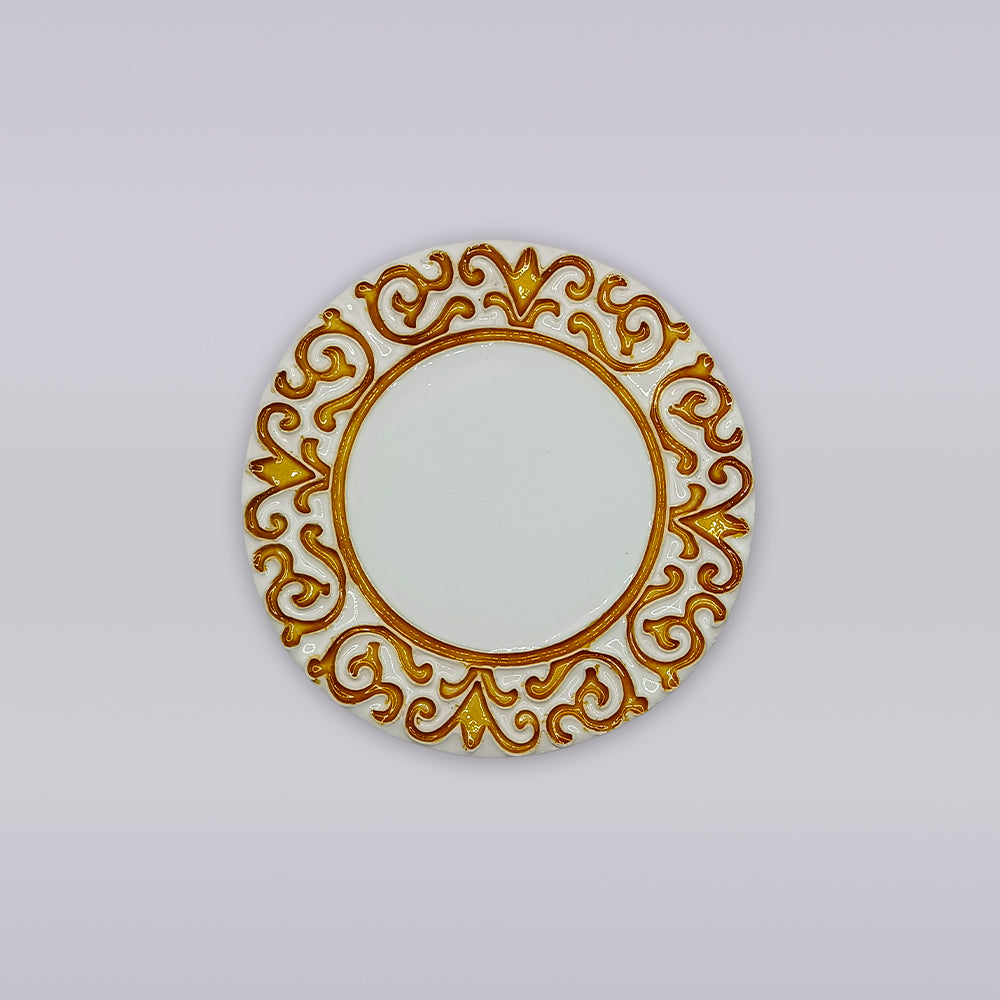 The Manueline Golden Crest Ceramic Coaster by Miradouro Ceramics features a round white design with an ornate gold and brown border of symmetrical swirls, inspired by Portuguese decor, displayed on a plain light gray background.