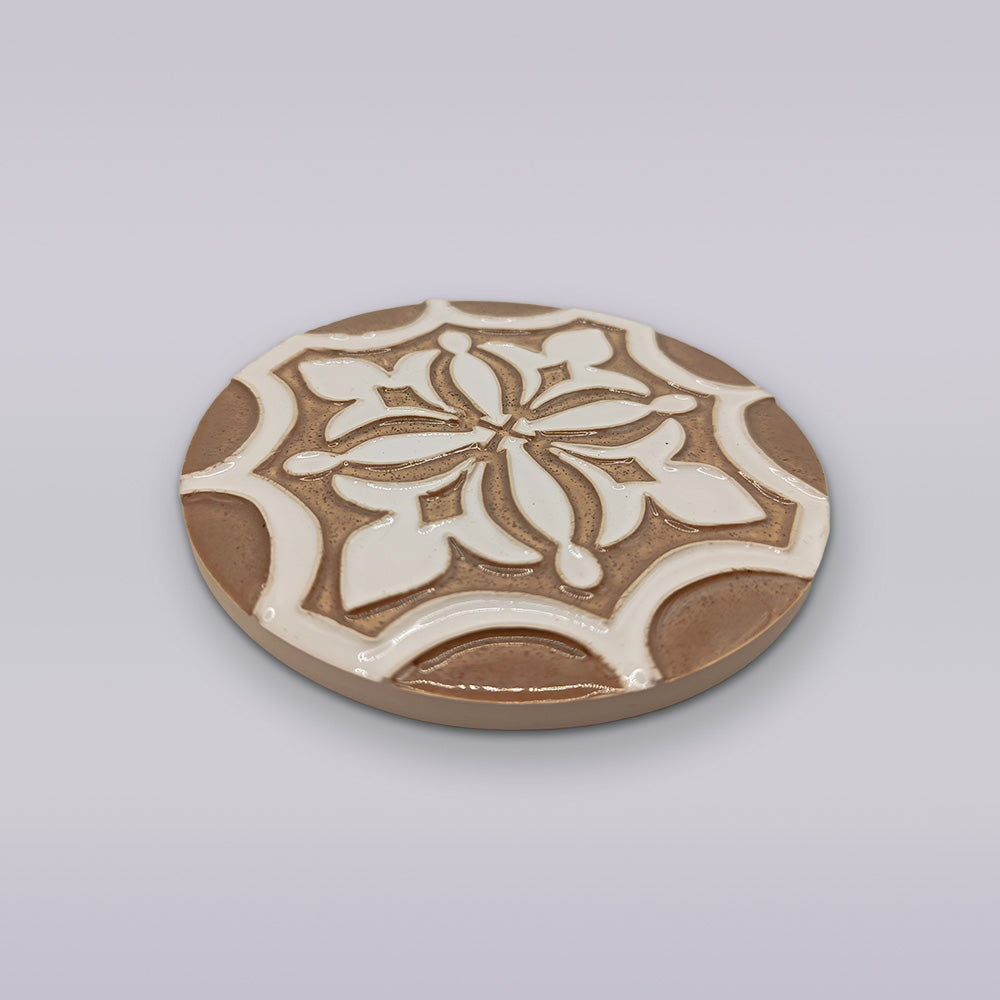 The Ocre Fleur by Miradouro Ceramics is a round Portuguese ceramic coaster with a raised floral and geometric pattern in brown and white on light gray, perfect for artisanal home décor.
