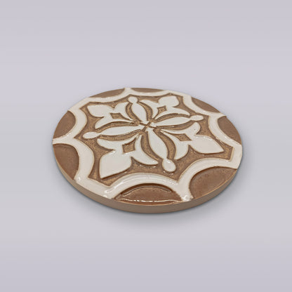 The Ocre Fleur by Miradouro Ceramics is a round Portuguese ceramic coaster with a raised floral and geometric pattern in brown and white on light gray, perfect for artisanal home décor.