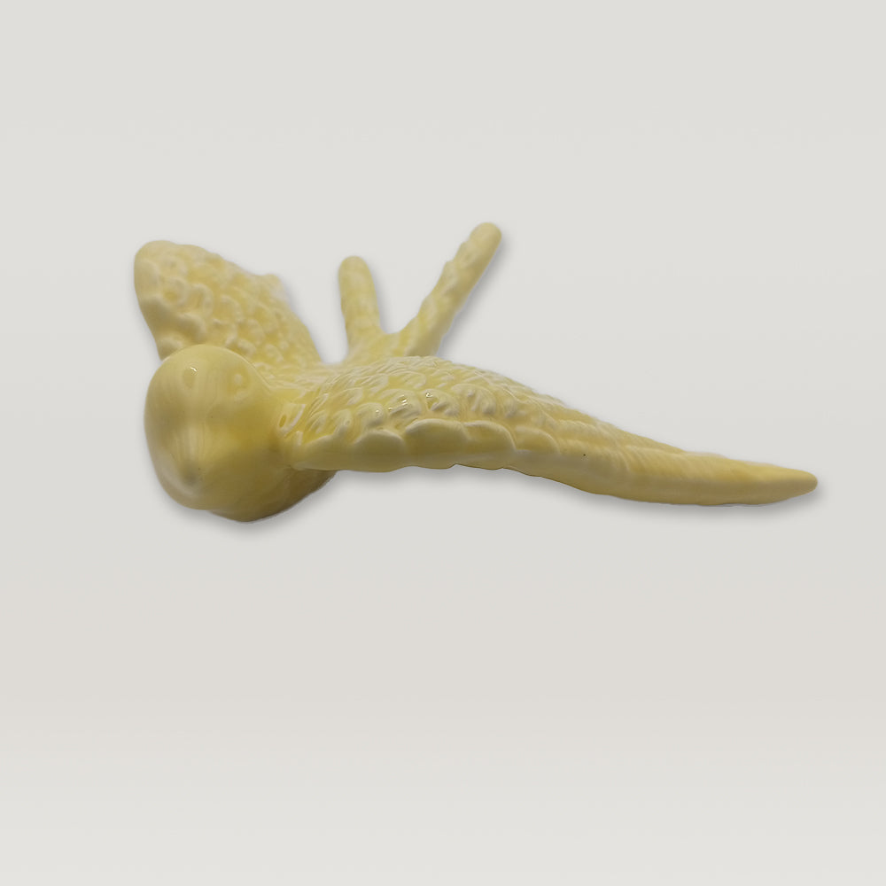 A yellow Tejo Shop Portuguese Ceramic Swallow is flying gracefully in an elegant manner on a white background.