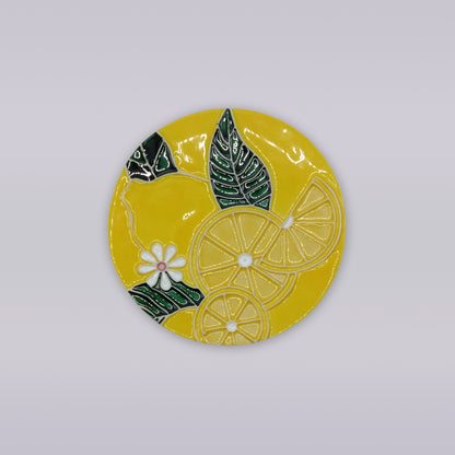 The Tejo Lemon Blossom Coaster – Ribatejo Edition by Miradouro Ceramics features sliced lemons, green leaves, and white flowers on a round yellow ceramic surface inspired by traditional Portuguese designs.