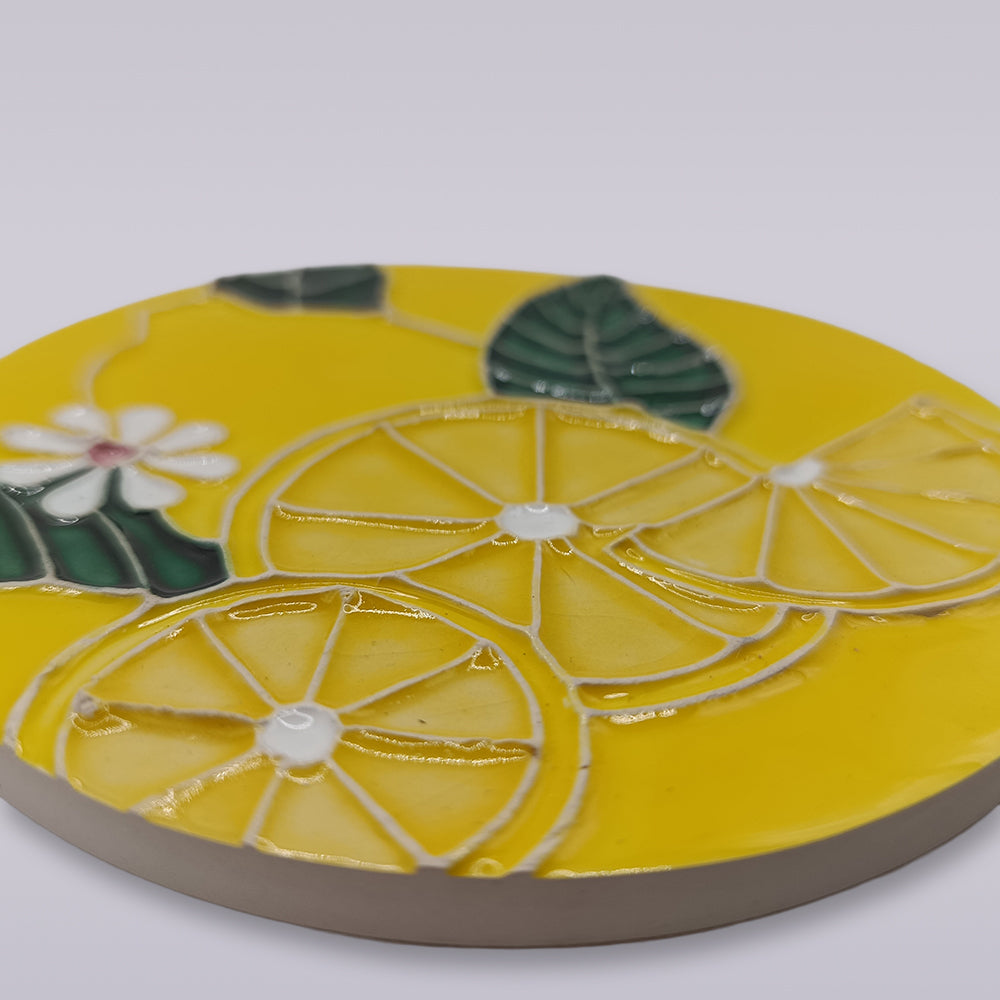 The Tejo Lemon Blossom Coaster – Ribatejo Edition by Miradouro Ceramics features a round, ceramic design with lemon slices, green leaves, and a white-yellow flower on a smooth, light background, inspired by Portuguese ceramic art.