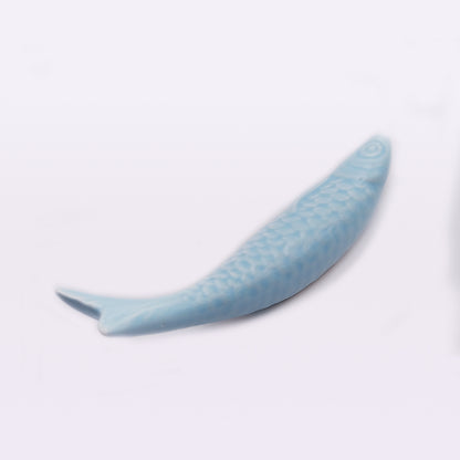 A light blue ceramic chopstick rest shaped like a fish is shown on a plain white background. The detailed pattern on its body, including scales and fins, showcases traditional craftsmanship. This exquisite piece of home decor evokes the charm of Portuguese Ceramic Sardines by Tejo Shop.