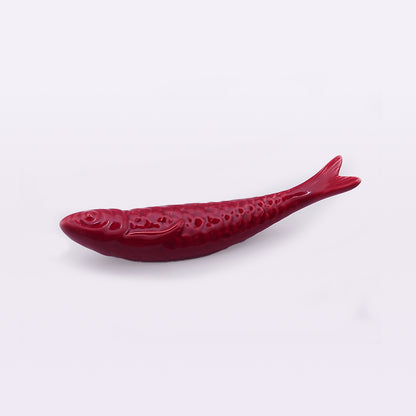 A small, red, decorative object shaped like a fish. The fish has a detailed texture including scales, fins, and facial features, reminiscent of handcrafted Portuguese ceramics. It appears to be made of a glossy, ceramic-like material and is set against a plain white background. This product is the Portuguese Ceramic Sardines by Tejo Shop.