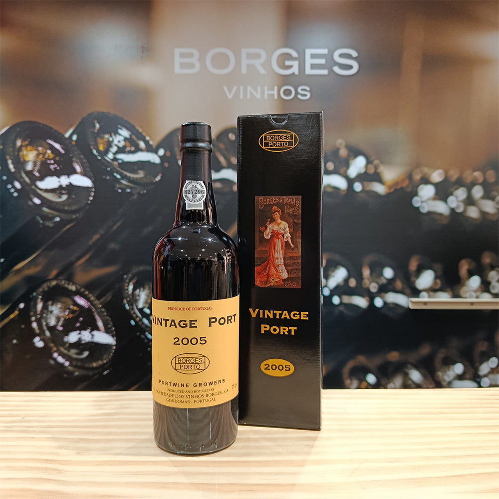 A bottle of Borges Vintage 2005 by Borges Wines rests on a wooden surface with its matching box. The background features the Borges Wines logo and stacked vintage wine bottles.