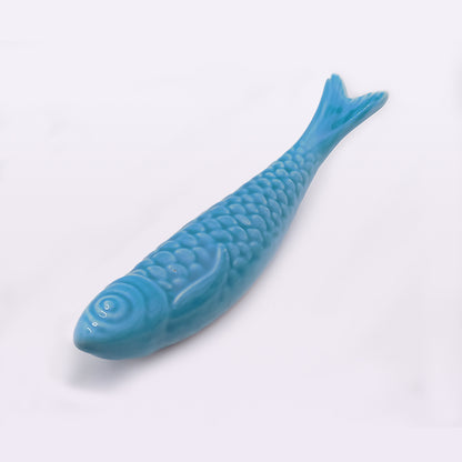 A blue, fish-shaped ceramic object with detailed scales and fins is displayed against a plain white background. The Portuguese Ceramic Sardines from Tejo Shop have raised eyes and a textured surface, showcasing traditional craftsmanship that makes them appear lifelike.