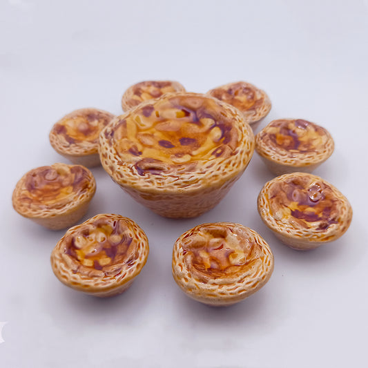 Eight miniature Ceramic Pastéis de Nata from Tejo Shop, each intricately detailed with a golden brown glaze, are elegantly arranged in a circle around a larger central tart. This charming setup is displayed against a plain white background, emphasizing the unique dimensions of each piece.