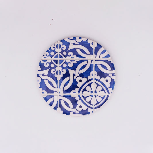 This hand-made Tejo Shop Coimbra Ceramic Tile Cup Pad features a round design with intricate blue and white geometric and floral patterns. Reminiscent of traditional tiles, the high-quality ceramic contrasts sharply against the plain, white background.