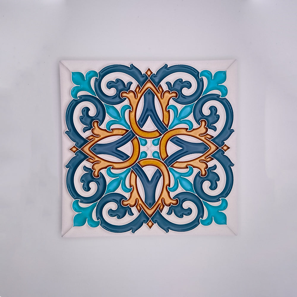 Handmade decorative ceramic tile with a symmetrical, intricate design featuring interlocking curves and floral motifs in shades of blue, gold, and brown, framed in white by Tejo Shop's hand-painted Tiles for Walls.