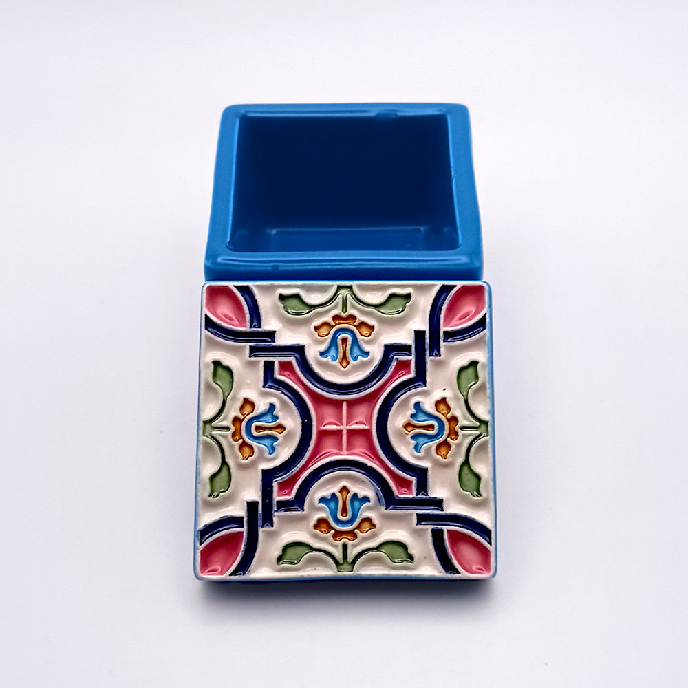 A small rectangular ceramic pot featuring artistic details in a vibrant, colorful geometric pattern on one side. The symmetrical design includes shades of pink, green, blue, and red. The top half is plain blue with an open compartment, making it an exquisite Tejo Shop Flowers Island Ceramic Box reminiscent of the Azores Islands' craftsmanship.