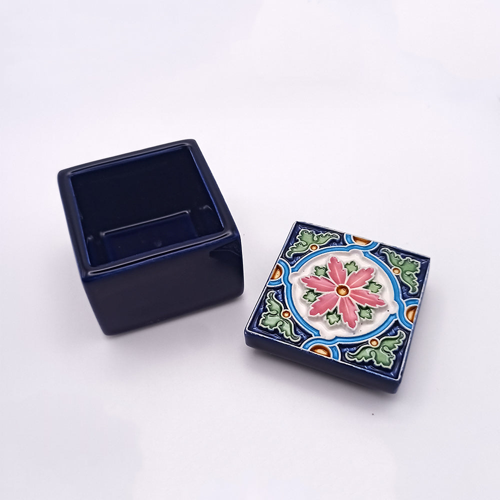 A small, square Graciosa Island Ceramic Box by Tejo Shop with its lid removed. The lid features a colorful floral design with pink, green, blue, orange, and white patterns. The box itself is dark blue, showcasing superb craftsmanship. The image is taken against a plain white background.