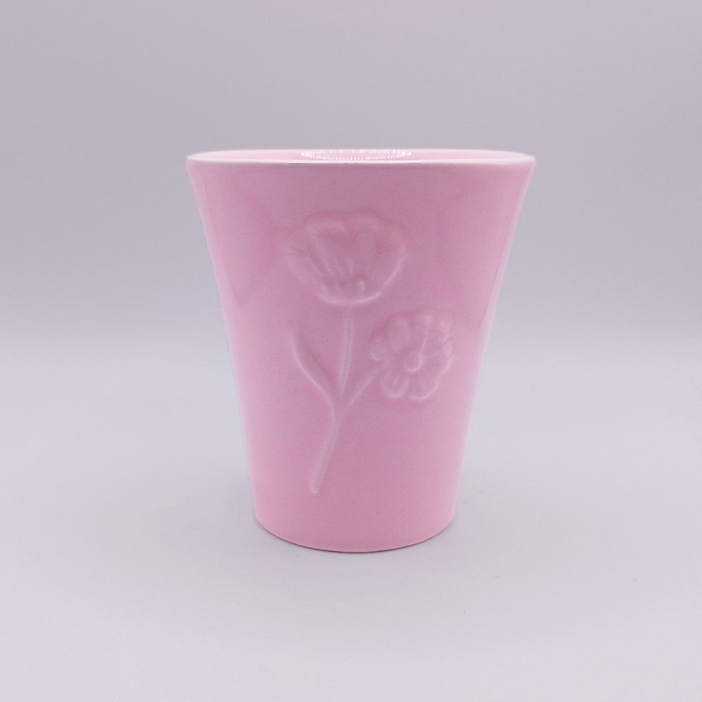 This unique ceramic mug from Tejo Shop features a pink color with embossed floral designs, showcasing the elegance of Portuguese art. The glossy finish and slightly flared top add to its charm. Set against a plain, light gray background, this handmade Ceramic Mug stands out as the focal point of the image.