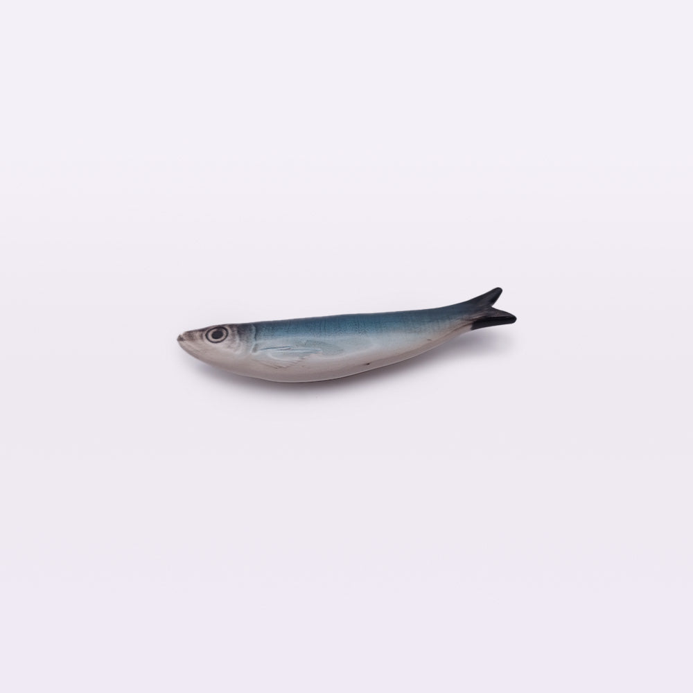 A realistic ceramic model of a fish, resembling a hand-made Portuguese ceramic sardine, mainly blue-gray in color with a white underbelly, lying against a plain light background—this is the Ceramic Sardine Fridge Magnet by Tejo Shop.